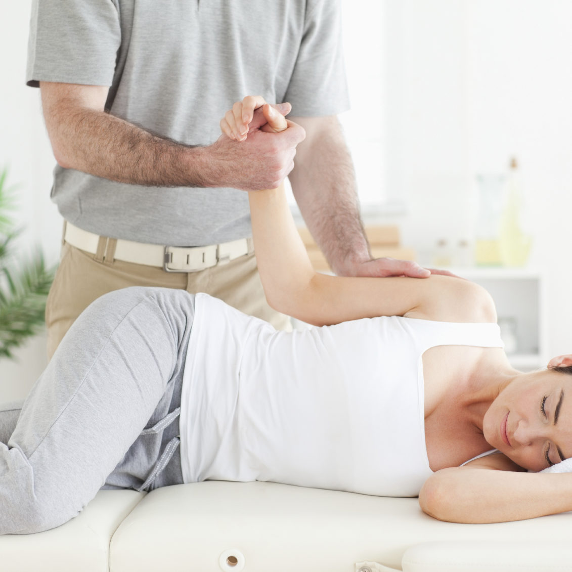 A chiropractor stretches a female customer's arm in his surgery